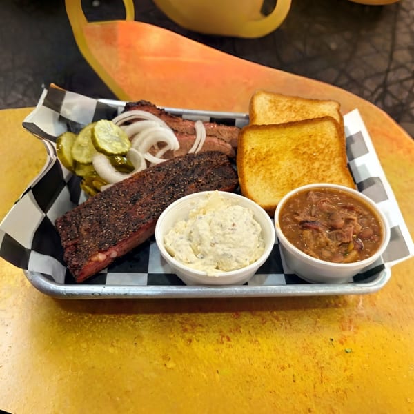 BBQ brisket and ribs with sides of potato salad, baked beans, pickles, onions, and toast.