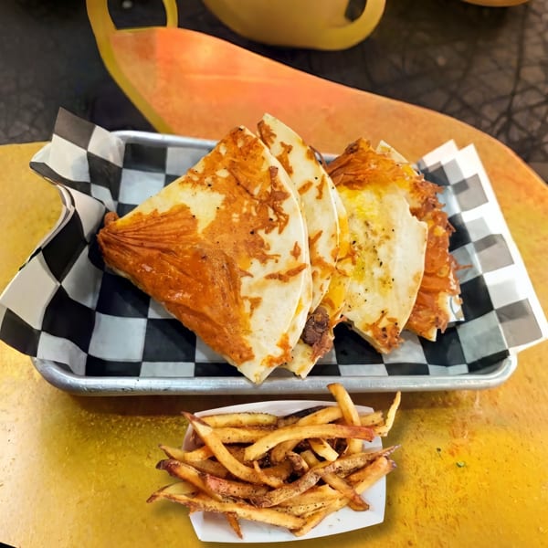 Four cheesy quesadilla slices in a checkered basket with a side of seasoned french fries.