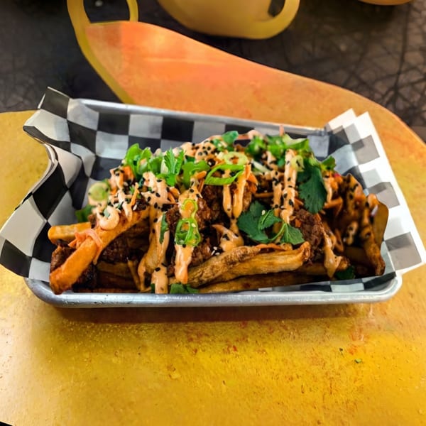 Loaded fries with meat, sauce, green onions, and sesame seeds in a metal tray.