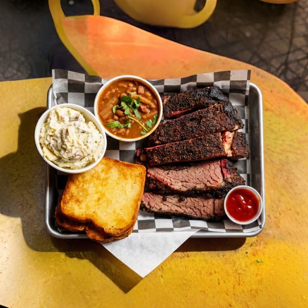 A metal tray with sliced brisket, baked beans, potato salad, toasted bread, and ketchup.